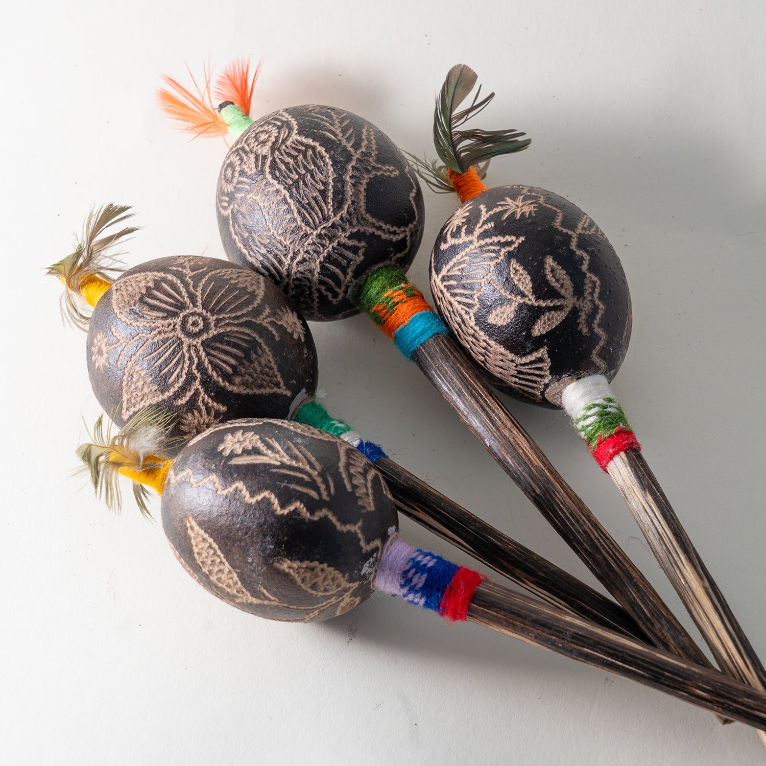 Vier schamanische Vogelrasseln mit Blumen- und Tiermotiv-Gravuren, buntem Federschmuck und verschiedenen Griffbaendern aus Peru