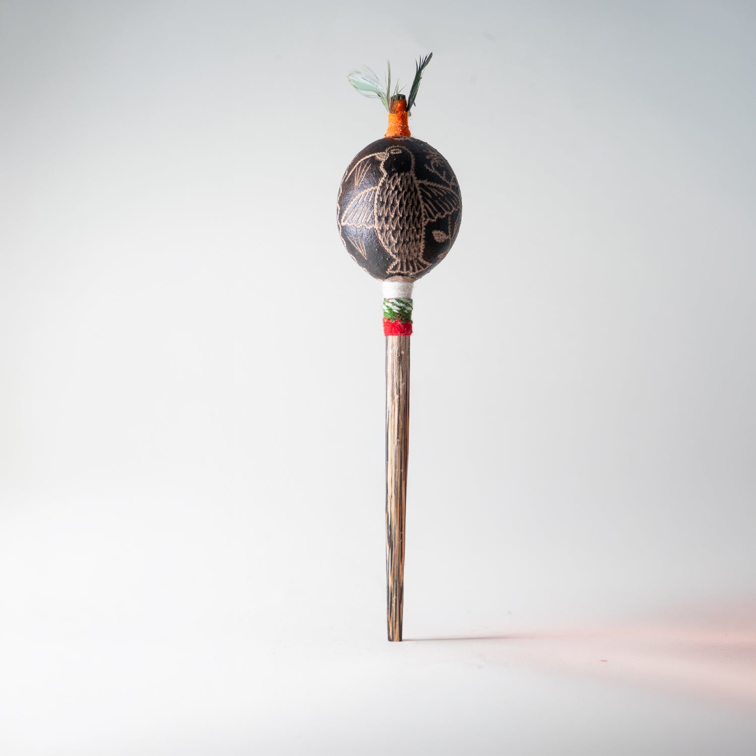 Schamanische Rassel mit eingraviertem Adler-Kondor-Motiv, grün-orangem Federschmuck und roSchamanische Rassel mit Adler-Gravur, gruen-orangem Federschmuck und rot-gruenem Griffband aus Perut-grünem Griffband – Ritualinstrument aus Peru